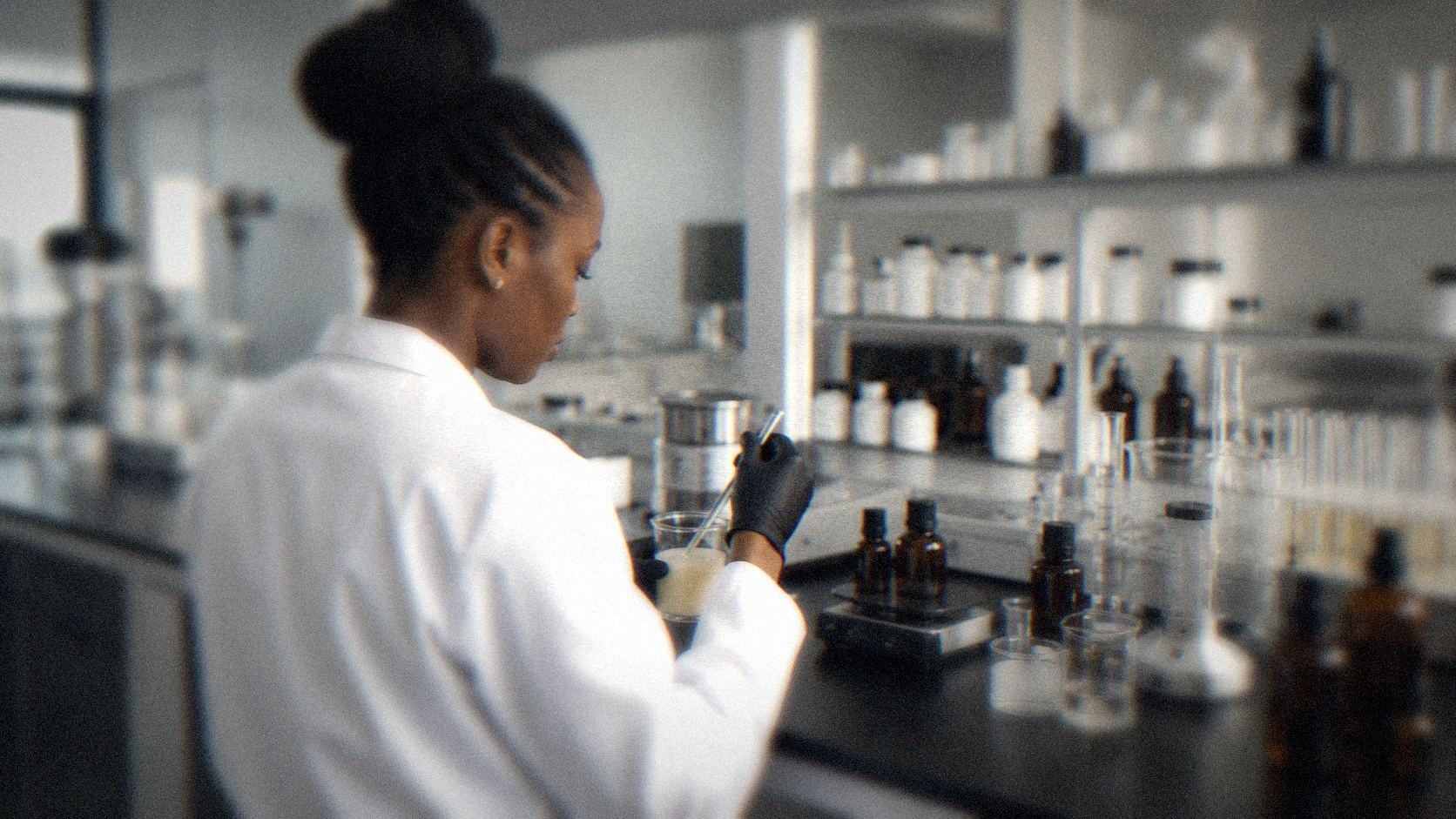 A cosmetics formulator testing a skincare sample in a lab, surrounded by glass and amber bottles