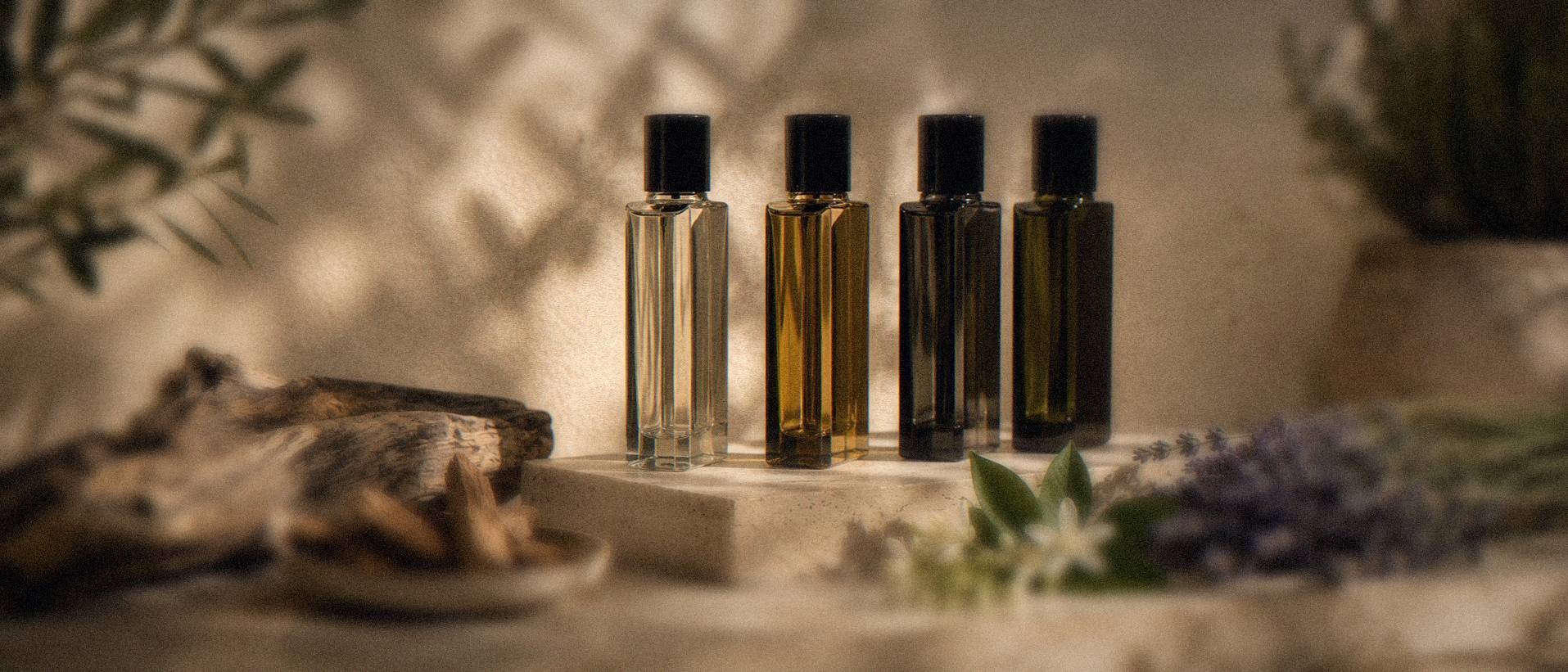 Four Matière Première fragrance bottles displayed outdoors with raw materials, sandalwood, lavender and orange blossom, arranged in front of them