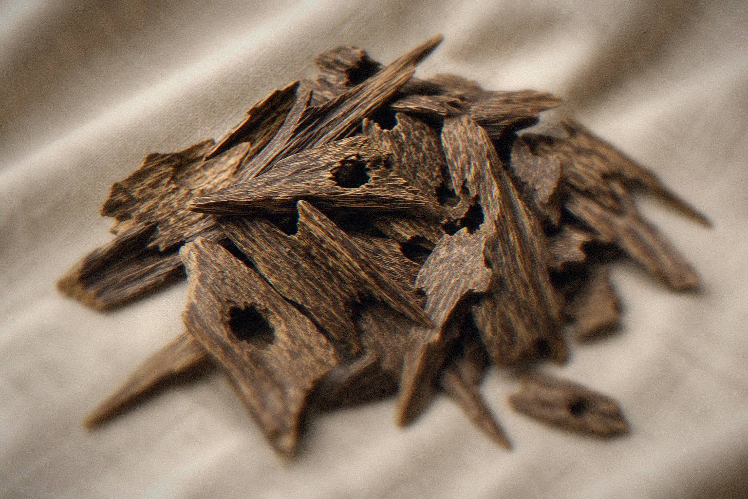 A pile of dark, resin-dense oud wood chips on natural linen fabric